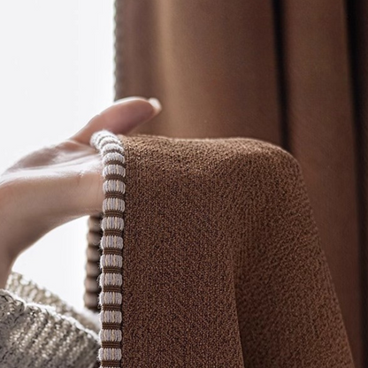 Hand holding textured brown curtain with decorative trim, close-up, home decor focus
