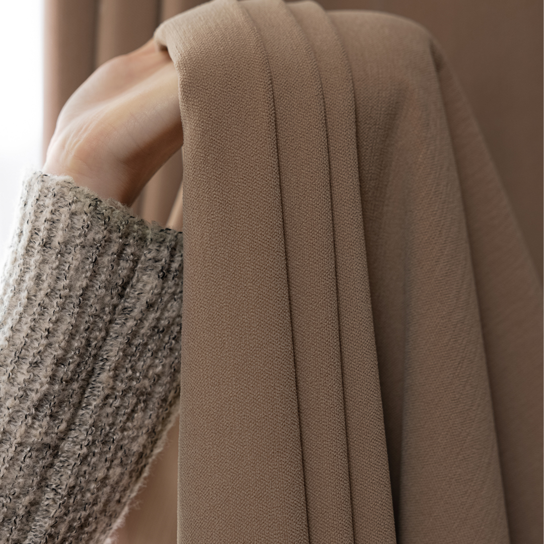 Close-up of hand holding deep walnut brown curtain fabric, textured home curtains