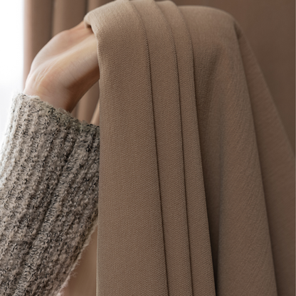 Close-up of hand holding deep walnut brown curtain fabric, textured home curtains