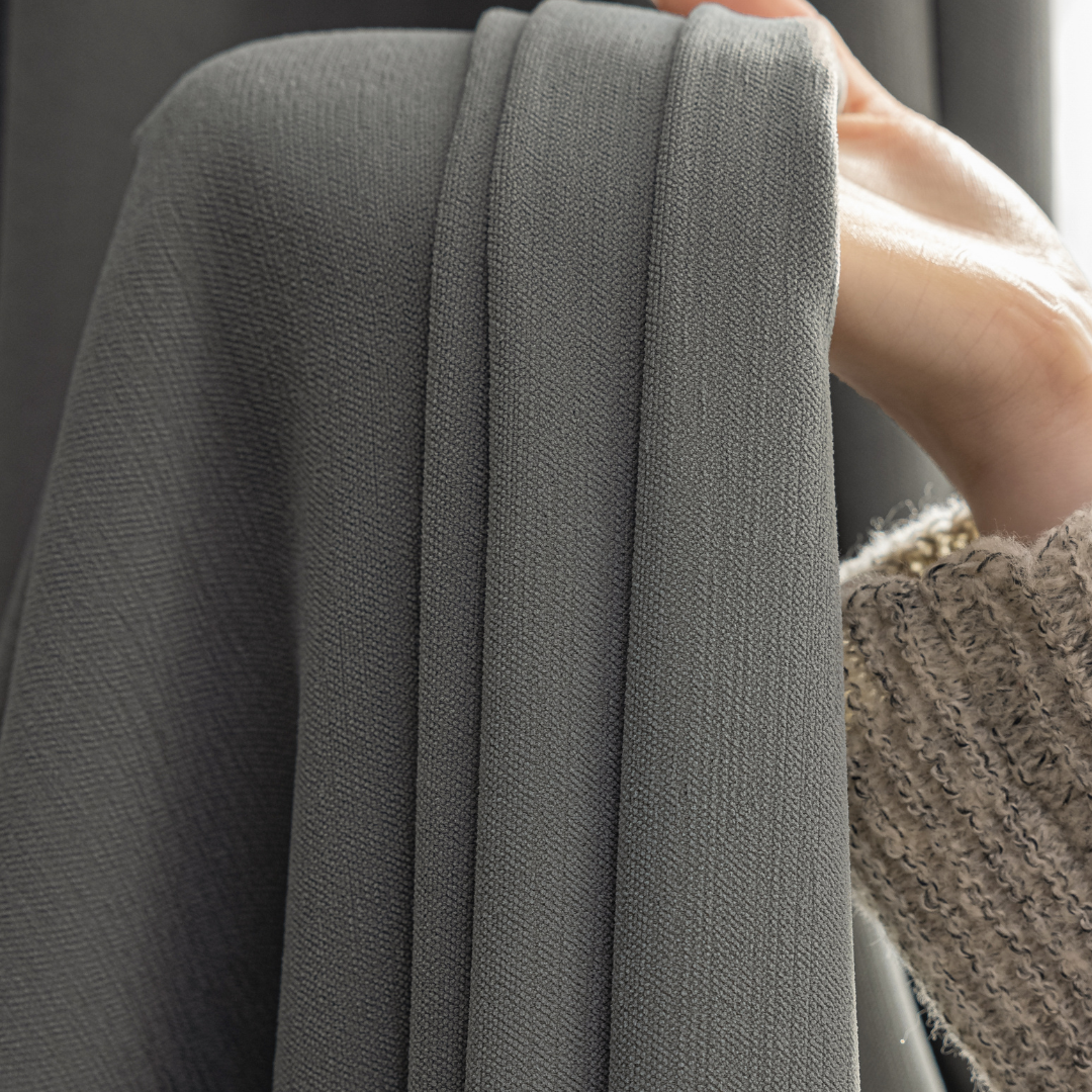 Hand holding soft textured graphite ash blackout curtain close up