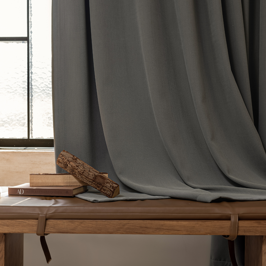 Graphite ash blackout curtain draped beside window, books, log on wooden bench