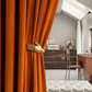 Luxe orange velvet blackout curtains with unique gold hand tieback in a modern living room