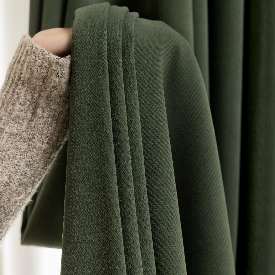 Hand holding dark green blackout curtain fabric, textured and pleated, close-up