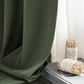 Dark green blackout curtain with sheer white curtain, decorative rope incense, and books on a glass table