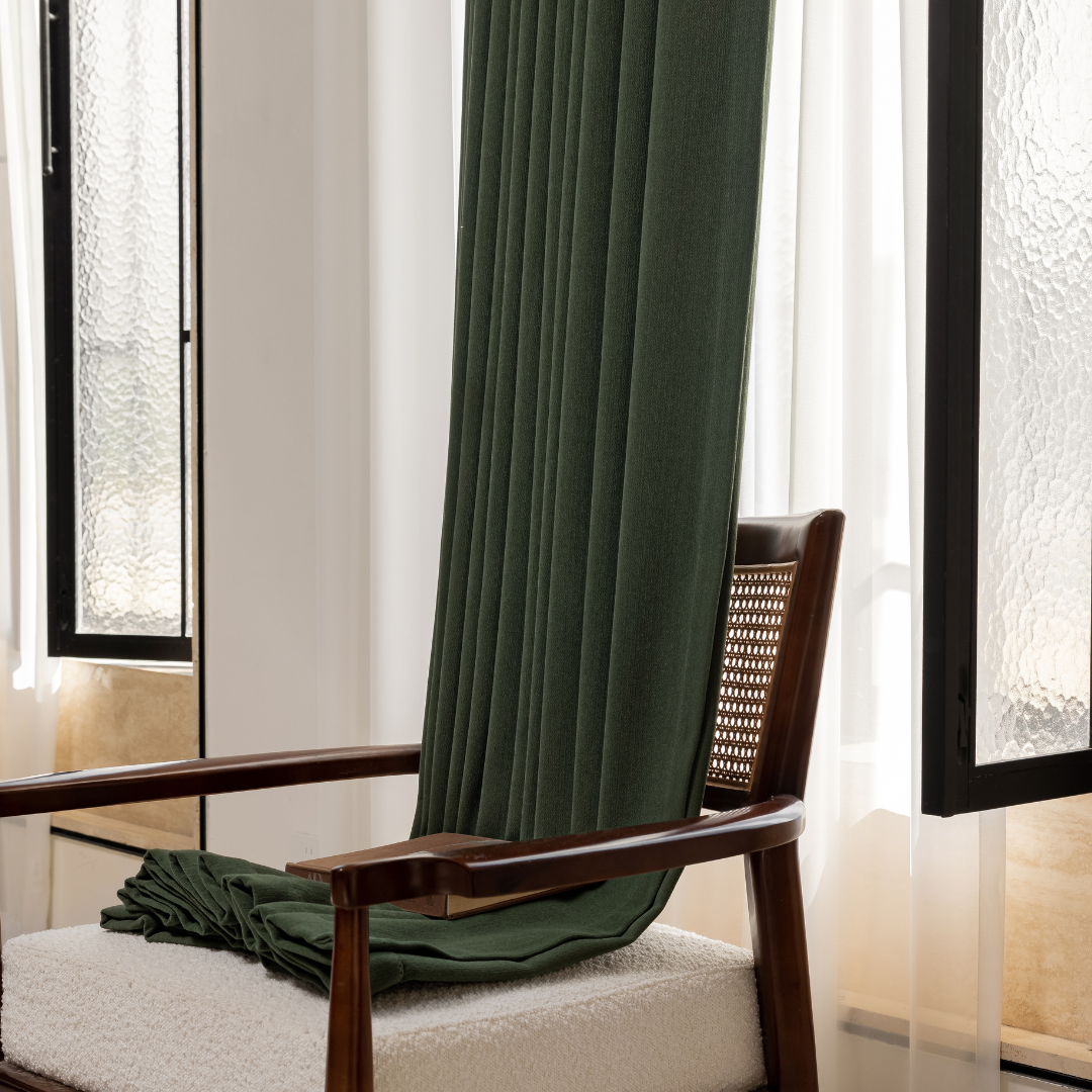 Dark green curtain fabric draped on a wooden chair near bright windows